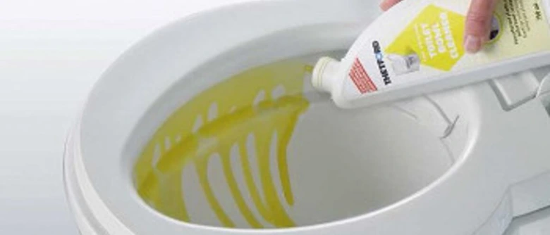 Ruka vylévá žlutou chemii do toalety.