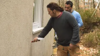 Muži opravují fasádu starého domu aplikací omítky.