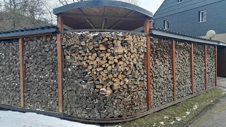 Dřevník s uspořádaným dřívím pod střechou venku.