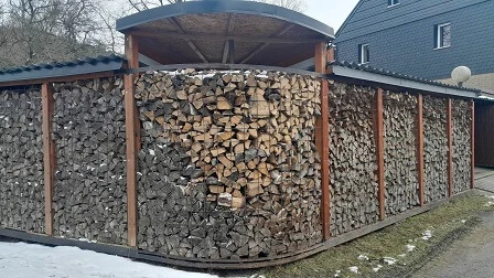 Hotový dřevník z kari sítě plný drahých polen pod střechou.