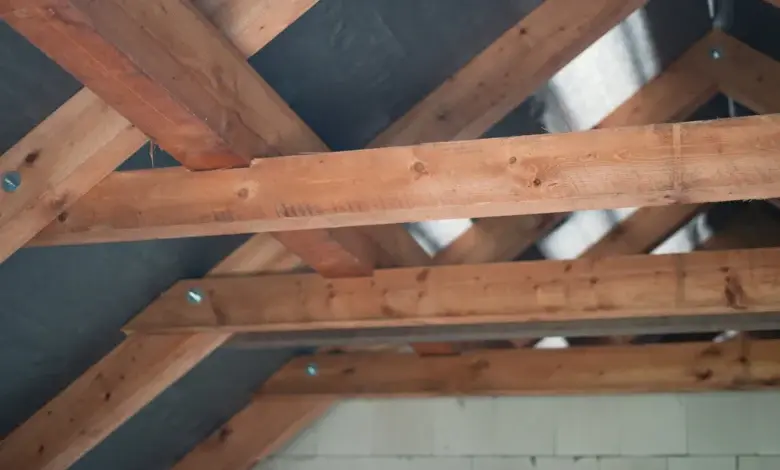 Dřevěné trámy střechy s viditelnými spoji a izolací pod nimi.