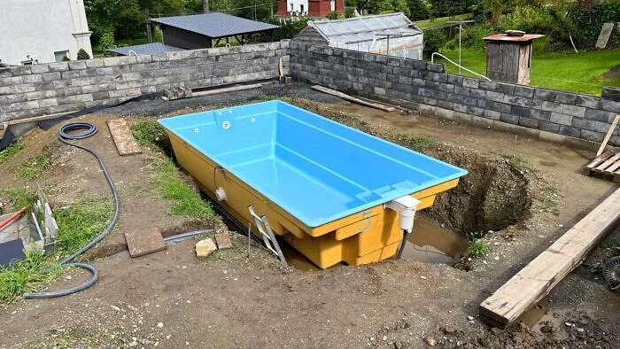 Zapuštěný bazén ve svahu s výkopem a opěrnými zdmi.
