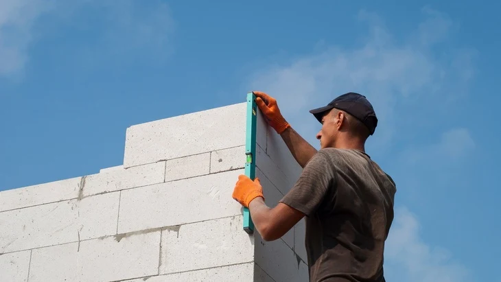 Stavebník vyrovnává roh z betonových bloků pomocí úrovně.