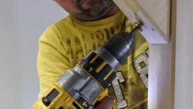 Muž v žlutém tričku šroubuje dřevěný trám pro pergolu.