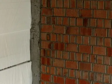 Bílý polystyren nalepený vedle cihlové zdi pro ukázku správného lepení.