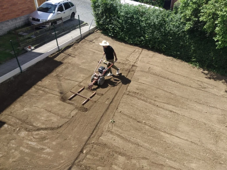 Muž srovnává zahradu motokultivátorem na slunci.