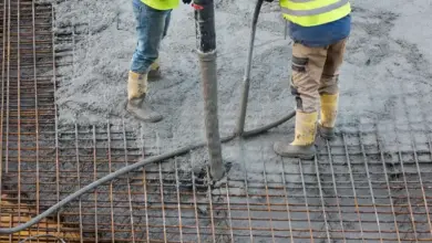 Dva dělníci nalévají beton na ocelovou mřížku do ztraceného bednění.