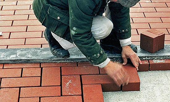 Muž kladne cihly na zahradní chodník s pravítkem.