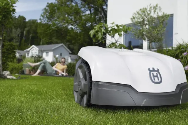 Bílá robotická sekačka kose trávu na zahradě.