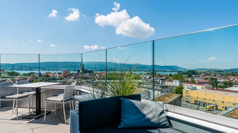 Moderní balkon s výhledem na město skrze bezpečnostní skleněné zábradlí.