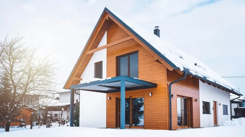 Modern dům s dřevěnou fasádou a zateplenými stěnami pod sněhem.