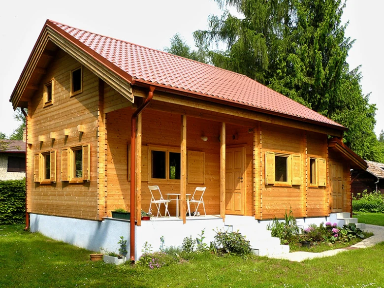 Dřevěná chata s červenou střechou na trámovém základu.