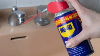 Ruka s sprejem WD-40 mazá mosazový kohout v koupelně.
