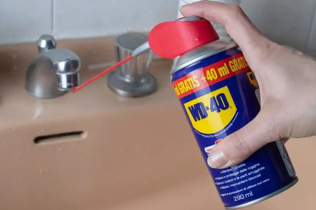 Ruka s sprejem WD-40 mazá mosazový kohout v koupelně.