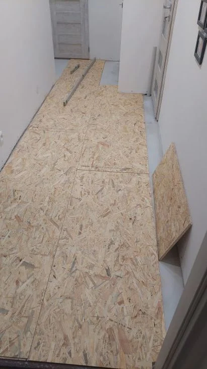 Instalace desek OSB na podlahu v chodbě s viditelnými spárami.