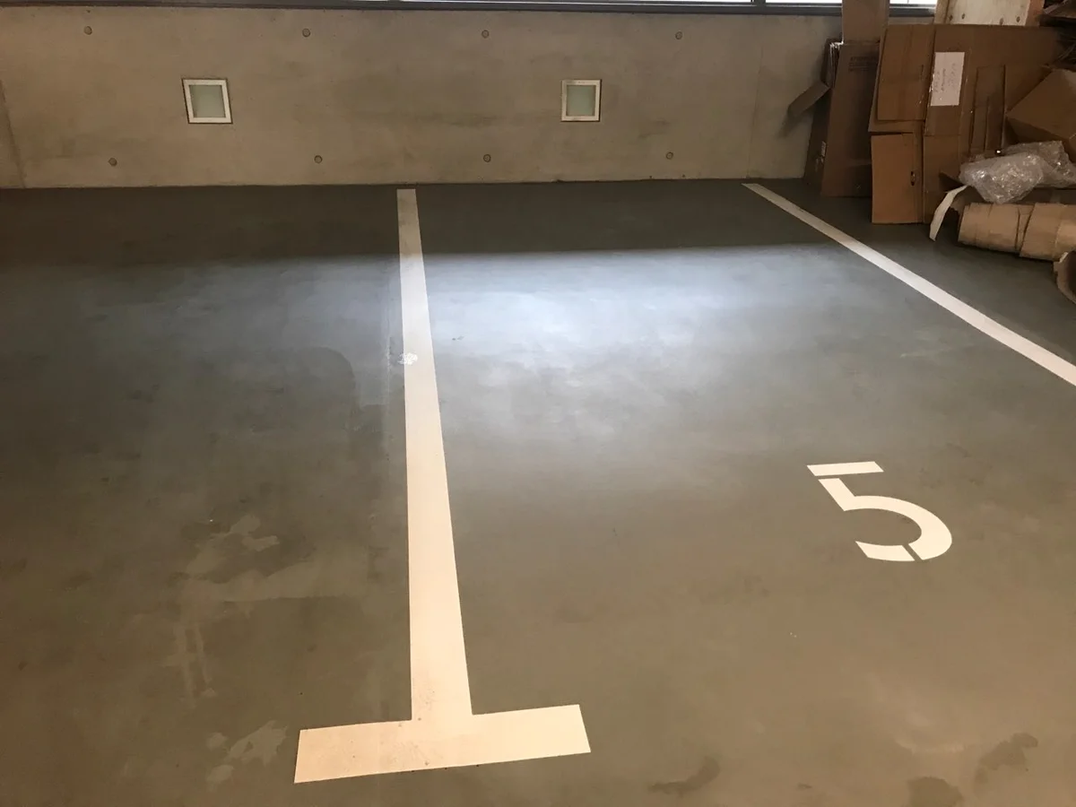 Kartáčovaný beton v garáži s bílými značkami pro parkování.