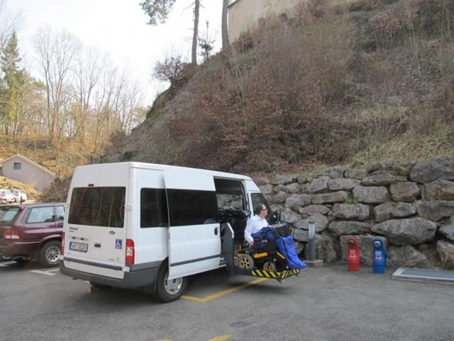 Bílý vozík pro invalidy zaparkovaný na vyhrazeném místě s rozloženým rampou.