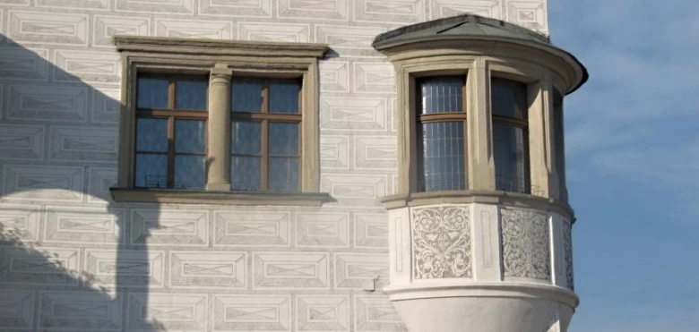 Bílá fasáda domu s arkýřem vedle obdélných oken.