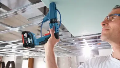 Muž montuje sádrokartonový strop pomocí elektrického šroubováku.