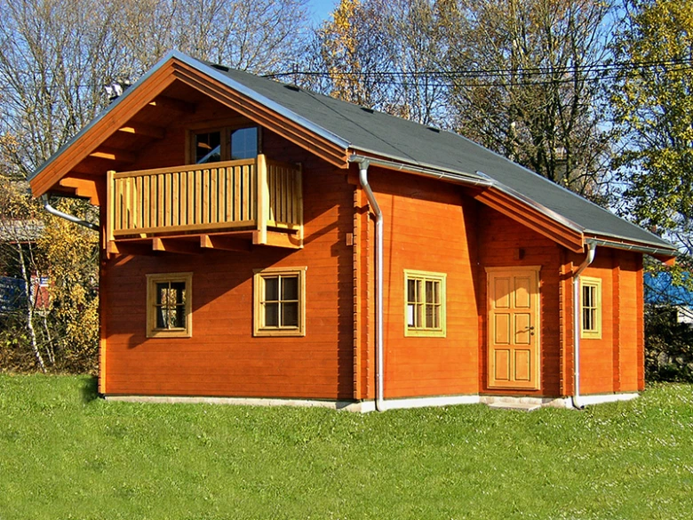 Dřevěná chata s balkónem na trávníku před stromy.