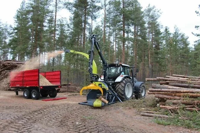 Traktor s drtičem zpracovává dřevo na štěpky v lese.