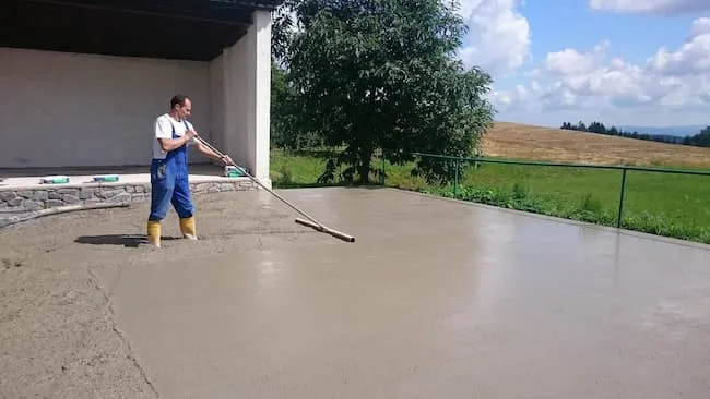 Muž hladí čerstvý beton na podlaze garáže nebo terasy.