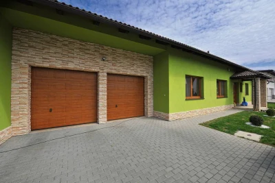 Modern dům s zelenou fasádou a garážemi na pozadí oblohy.