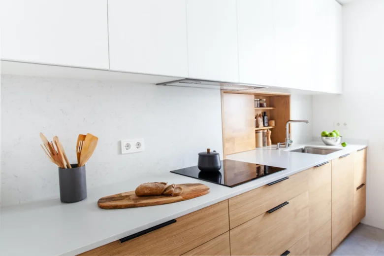 Bílá kuchyně s dřevěnými skříněmi a pracovní deskou.