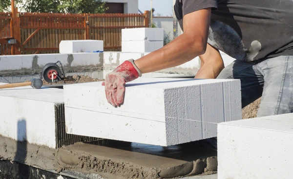 Stavebník položí velký izolovaný betonový blok na maltu.