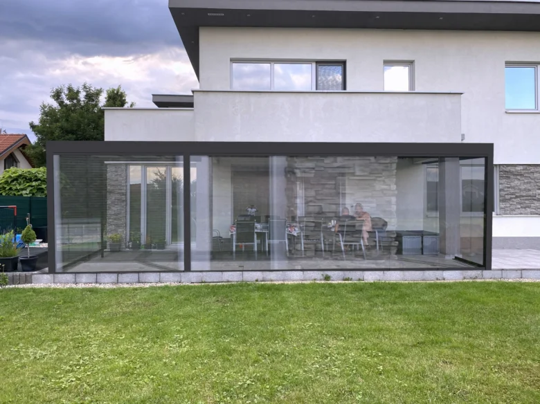 Moderní skleněná pergola připojená k domu s výhledem na zahradu.
