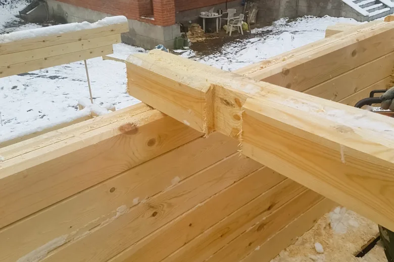 Detail spoje dřevěných trámů na stavbě v zimním prostředí.