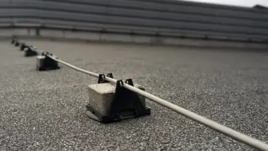 Zemní vodič hromosvodu na ploché střechě s betonovými závažími.