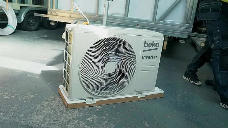 Venkovní jednotka klimatizace značky Beko na kartonu v dílně.