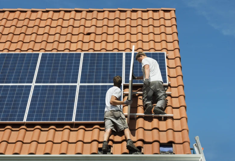 Dva dělníci montují fotovoltaické panely na střechu domu.