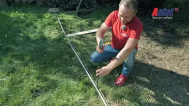 Muž kladoucí dřevěný plot pomocí špice na trávníku.