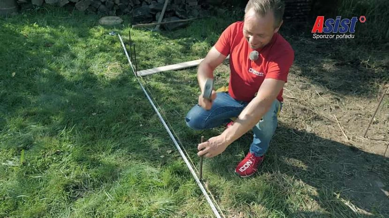 Muž kladoucí dřevěný plot pomocí špice na trávníku.