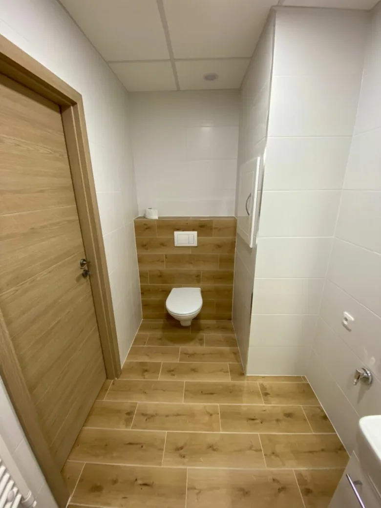 Moderní koupelna s bílými stěnami a dřevěnými prvky na podlaze.