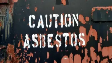 Varovný nápis CAUTION ASBESTOS na zdi s odlupující se barvou.