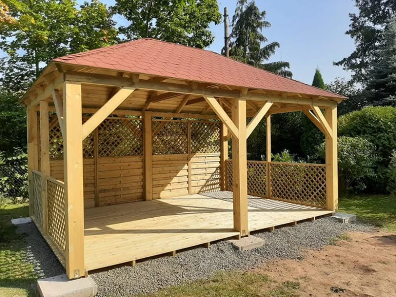 Nová dřevěná zahradní pergola s červenou střechou na štěrku.