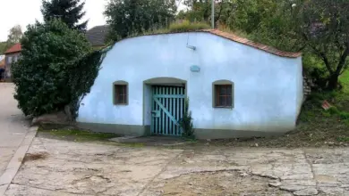 Bílý sklep v zemi s modrou vratou a okny.