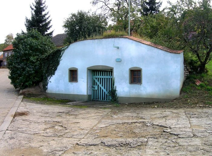 Bílý sklep v zemi s modrou vratou a okny.