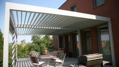 Bílá kovová pergola u červené cihlové domu s venkovním jídelním setem.