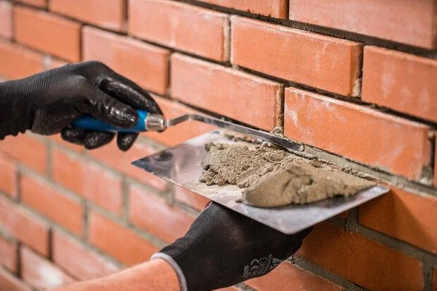 Stavebník nanáší maltu mezi cihly pomocí špachtle.