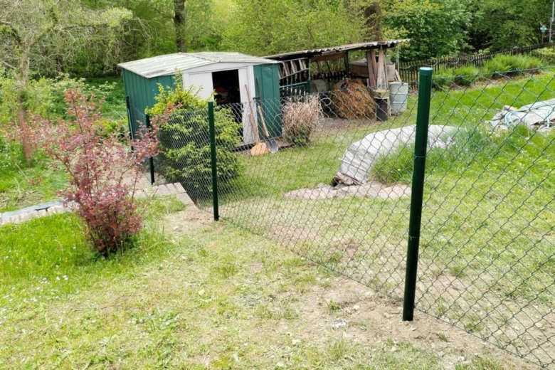 Plot na svahu s plotem, stodolou a zahradním pozemkem.