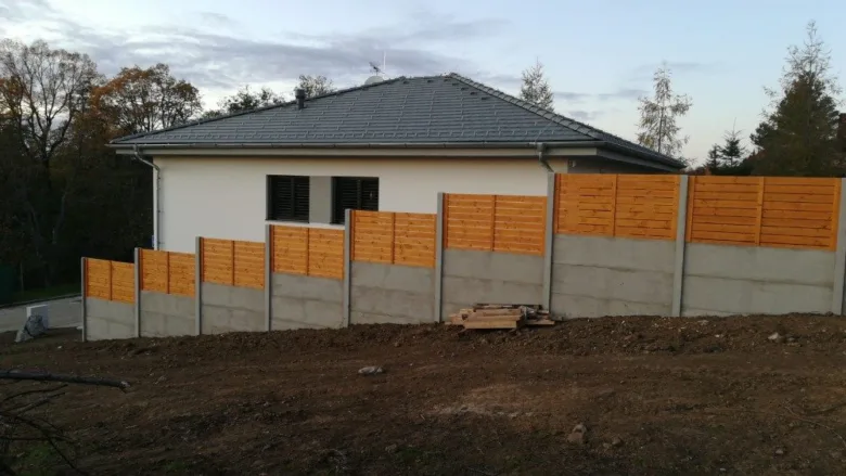 Nový betonový plot s dřevěnými prvky na svahu u domu.