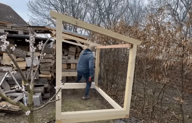 Muž staví dřevěný rám pro skladování paliva venku.