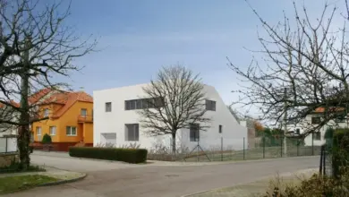 Moderní bílý dům s velkými okny v rezidenční čtvrti pod modrou oblohou