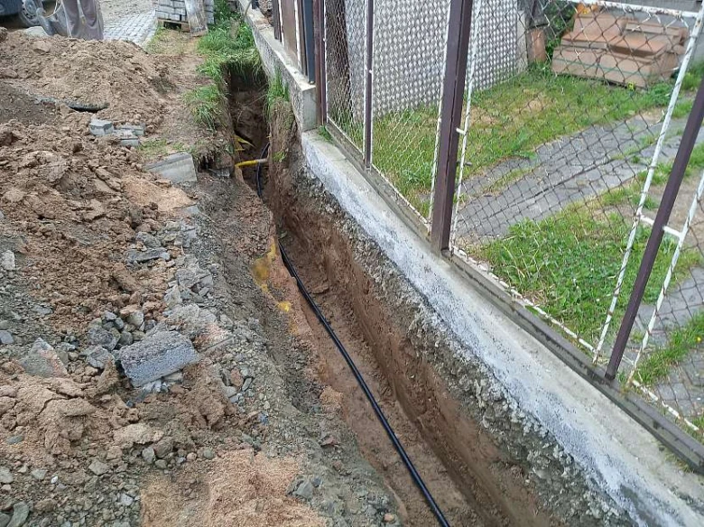 Výkop pro vodovodní přípojku s položenými potrubím.