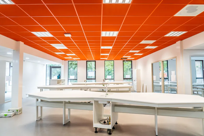Oranžové akustické podhledy v laboratoři s bílými pracovními stoly.