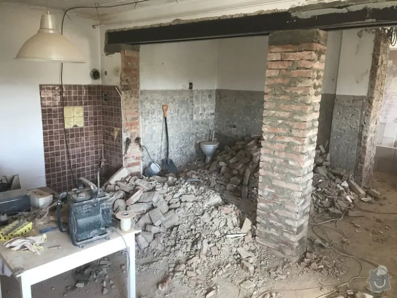 Interiér v rekonstrukci s hromadou sutiny a odhalenými cihlovými sloupy.